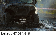 A powerful off-road vehicle splashes through a muddy puddle, creating a cloud of spray and casting a dark shadow. The vehicle is equipped with large tires and a roll cage for extreme off-roading. Стоковое фото, фотограф Воловодов Владимир / Фотобанк Лори