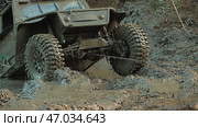 A close-up of an SUV stuck in a muddy hole. The SUV is at an angle, its rear wheels sinking into the mud. A winch cable is attached to the car, an attempt to pull the car out. Стоковое фото, фотограф Воловодов Владимир / Фотобанк Лори