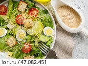 Тарелка с вкусным салатом Цезарь и соусником на белом фоне, крупным планом. Стоковое фото, фотограф Pixel_shot / Фотобанк Лори
