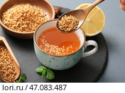 Женская рука с чашкой горячего гречишного чая, листья мяты, деревянная ложка и лимон на сером фоне. Стоковое фото, фотограф Pixel_shot / Фотобанк Лори