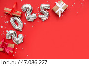 Цифры 2025 из фольгированных шаров с рождественскими подарочными коробками и конфетти на красном фоне. Стоковое фото, фотограф Pixel_shot / Фотобанк Лори