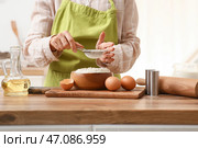 Женщина просеивает муку для приготовления теста на кухонном столе. Стоковое фото, фотограф Pixel_shot / Фотобанк Лори