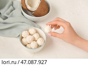 Женщина берет вкусную кокосовую конфету из миски на белом столе. Стоковое фото, фотограф Pixel_shot / Фотобанк Лори