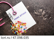 Бумага с текстом ПАНИЧЕСКАЯ АТАКА, стетоскоп и рассыпанные таблетки на сером фоне. Стоковое фото, фотограф Pixel_shot / Фотобанк Лори
