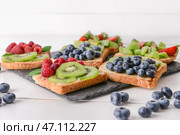 Грифельная тарелка с вкусными бутербродами, киви и ягодами на белом столе. Стоковое фото, фотограф Pixel_shot / Фотобанк Лори