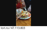 A waiter uses scissors to cut a lobster for customers at a restaurant in Nha Trang, Vietnam. Lobster baked with cheese and garlic is served with vegetables. Vertical video, real time. Selective focus. Стоковое видео, видеограф Наталья Любина / Фотобанк Лори