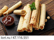 Доска с вкусными вафельными трубочками, вареной сгущенкой и фундуком на коричневом деревянном фоне. Стоковое фото, фотограф Pixel_shot / Фотобанк Лори