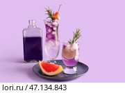 Бутылка с бокалами холодного джина и тоника на фиолетовом фоне. Стоковое фото, фотограф Pixel_shot / Фотобанк Лори