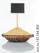 Plate with a bunch of millet grains and its reflection and price tag, pointer. Стоковое фото, фотограф Александр Собко / Фотобанк Лори