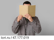 Молодой человек, закрывающий лицо, читая книгу на сером фоне. Стоковое фото, фотограф Pixel_shot / Фотобанк Лори