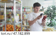 Interested young guy standing in grocery store aisle with ketchup in hand, scanning barcode on bottle with smartphone to get information about product. Modern technologies for shopping. Стоковое видео, видеограф Яков Филимонов / Фотобанк Лори