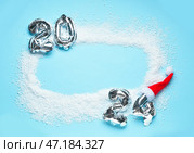 Рамка из серебристых фольгированных шаров с номером 2024, снег и шапка Санты на голубом фоне. Концепция Нового года. Стоковое фото, фотограф Pixel_shot / Фотобанк Лори