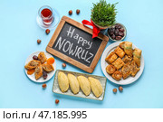 Доска с текстом HAPPY NOWRUZ, угощения, стакан чая и травы на синем фоне. Стоковое фото, фотограф Pixel_shot / Фотобанк Лори