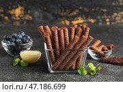Стеклянная миска с вкусными шоколадными вафельными трубочками, сгущенным молоком и черникой на черном столе на деревянном фоне. Стоковое фото, фотограф Pixel_shot / Фотобанк Лори