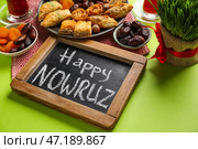 Доска с текстом HAPPY NOWRUZ, угощения и трава на зеленом фоне, крупным планом. Стоковое фото, фотограф Pixel_shot / Фотобанк Лори