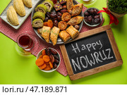 Доска с текстом HAPPY NOWRUZ, угощения, стакан чая и травы на зеленом фоне. Стоковое фото, фотограф Pixel_shot / Фотобанк Лори