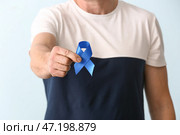 Человек с голубой лентой на цветном фоне, крупным планом. Концепция рака толстой кишки. Стоковое фото, фотограф Pixel_shot / Фотобанк Лори