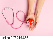 Женские руки с красным сердцем и стетоскоп на цветном фоне. Кардиологическая концепция. Стоковое фото, фотограф Pixel_shot / Фотобанк Лори