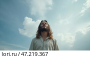 Man with long hair is standing in a field with a blue sky above him. Стоковое AI-изображение, AI-художник Sergey Grishin / Фотобанк Лори