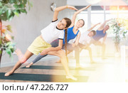 Middle-aged woman, man, preteen girl and boy practicing Extended Side Angle Pose or Utthita Parsvakonasana on mats during family Hatha yoga class in studio. Стоковое фото, фотограф Яков Филимонов / Фотобанк Лори