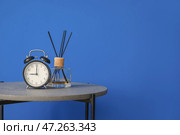 Стильный столик с язычковым рассеивателем и часами у цветной стены. Стоковое фото, фотограф Pixel_shot / Фотобанк Лори