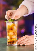 Женщина-бармен кладет мяту в стакан вкусного коктейля Cuba Libre на стол в баре. Стоковое фото, фотограф Pixel_shot / Фотобанк Лори