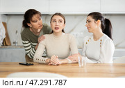 Sad woman sits silently in kitchen, adult girls sympathize and comfort her. Стоковое фото, фотограф Яков Филимонов / Фотобанк Лори