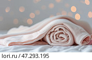 Soft, rolled pastel blanket on a bed with warm bokeh lights in the background creates a cozy atmosphere. Стоковое AI-изображение, AI-художник Сергей Толмачёв / Фотобанк Лори
