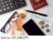 На столе полис ОМС, паспорт гражданина России, смартфон, наличные деньги рубли и калькулятор. Бизнес натюрморт (2018 год). Редакционное фото, фотограф Sergei Gorin / Фотобанк Лори
