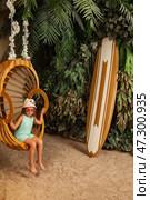 Seven Year Old Girl Model in Stylish Outdoor Swing With Tropical Decor and Surfboard. Стоковое фото, фотограф Aleksandr Golubev / Фотобанк Лори