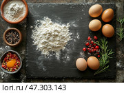 Ingredients for a meal laid out on a dark stone surface. In the center is crumbly flour, next to which are brown eggs, fresh red berries and sprigs of rosemary. Wooden bowls contain spices, including black pepper and dried herbs, as well as a bowl with a raw egg yolk and additives. The composition looks aesthetically pleasing, conveying an atmosphere of home comfort, culinary creativity and natural products. Стоковое AI-изображение, AI-художник Анна Кривицкая / Фотобанк Лори