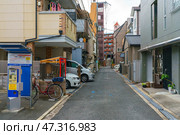 Osaka, Japan - Sep 23 2024, panoramic view of a narrow quite street in a residential area of the city with parked cars, apartment buildings and a payphone, cloudy day, no people, Osaka, Japan. Редакционное фото, фотограф Сергей Богомяко / Фотобанк Лори