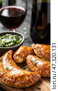 Plate of Argentine empanadas with golden crusts served with chimichurri sauce and a glass of Malbec wine on a rustic table. Стоковое AI-изображение, AI-художник 123 12 / Фотобанк Лори
