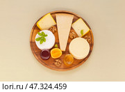 Various types of hard and soft cheeses with basil, honey, fruit jam and walnuts on wooden plate on light table. Organic nutritious products. Top view, close-up, flat lay, mock up, copy space. Стоковое фото, фотограф Виктория Катьянова / Фотобанк Лори