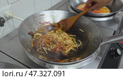 Cooking delicious stir-fried noodles with vegetables and meat in a busy kitchen setting in the evening. Стоковое видео, видеограф Сергей Толмачёв / Фотобанк Лори
