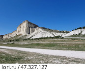 The majestic White Rock (Ak-Kaya), located in Crimea, near the town of Belogorsk. This is one of the most recognizable and picturesque natural wonders of the peninsula. Snow-white limestone cliffs rise above the steppe valley, creating a contrast between the bright blue sky, dry grasses and light rocks. The rock looks monumental, as if it keeps ancient secrets - it really has archaeological and historical significance.White Rock (Ak-Kaya) is a limestone cliff about 100 meters high, formed in the Cretaceous period. This is a place of archaeological finds, legends, filming and inspiration for artists and poets. Стоковое фото, фотограф Анна Кривицкая / Фотобанк Лори