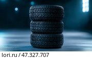 Four new tires stacked in a dark workshop setting with soft lighting. В тускло освещенной мастерской стоит стопка из четырех новых шин. Гладкий рисунок протектора и контуры видны, подчеркивая их качество и дизайн. Стоковое AI-изображение, AI-художник Katsiaryna Repich / Фотобанк Лори
