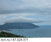 A picturesque view of Gurzuf from above. In the center of the composition is the majestic Mount Ayu-Dag, covered with a thick cap of clouds, like a magic veil. Below is the coast with houses, hotels and a bay in which the famous Adalary rocks are visible, like two guards at the entrance to the sea. Everything is surrounded by dense Crimean forests and greenery, creating a feeling of silence, peace and harmony. The atmosphere is filled with cool freshness, the breath of the sea and the anticipation of something new. Стоковое фото, фотограф Анна Кривицкая / Фотобанк Лори