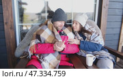 Couple relaxing on a patio wrapped on checkered blankets. Relaxed beautiful woman with a handsome man sitting on wooden cottage terrace. Winter resort. Happy loving couple enjoying leisure, embracing. Стоковое видео, видеограф Марина Демидюк / Фотобанк Лори