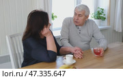 Old couple have breakfast sitting at the kitchen table, drink coffee. Embracing elderly man and woman. Senior couple together marriage in retirement talking with each other. Enjoying the pleasantries. Стоковое видео, видеограф Марина Демидюк / Фотобанк Лори