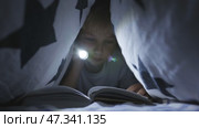 A little boy reads a book with a flashlight under the covers at night. Стоковое видео, видеограф Mikhail Davidovich / Фотобанк Лори