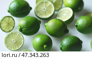 Fresh limes scattered on a white surface with some cut in half to reveal vibrant green insides and textured skin. Стоковое AI-изображение, AI-художник Сергей Толмачёв / Фотобанк Лори