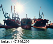 The image captures three large cargo vessels berthed at a bustling port, surrounded by cranes and reflecting sunlight, emphasizing the efficient maritime logistics operations. Стоковое AI-изображение, AI-художник Sergey Grishin / Фотобанк Лори