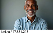 An older man with grey beard smiles brightly, showing warmth and approachability. He wears a denim shirt and has his arms crossed in a casual pose against a neutral gray background. Black african man. Стоковое AI-изображение, AI-художник Sergey Grishin / Фотобанк Лори