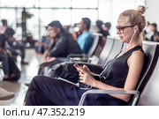 Female traveler using her cell phone while waiting to board a plane at departure gates at asian airport terminal. Стоковое фото, фотограф Matej Kastelic / Фотобанк Лори