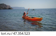 A woman is paddling a kayak in the ocean. The water is calm and the sky is clear. Стоковое видео, видеограф svetograph / Фотобанк Лори