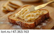 A thin, even layer of golden butter being spread on a rustic sourdough toast. Намазывание масла на тост: Тонкий крупный план тонкого ровного слоя золотистого сливочного масла, нанесенного на тост из деревенской закваски матово-золотистым ножом. Поверхность тоста хрустящая, текстурированная, с крошечными воздушными карманами. Стоковое AI-изображение, AI-художник Katsiaryna Repich / Фотобанк Лори