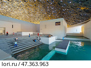Abu Dhabi, United Arab Emirates - Jan 17 2024, Panoramic view of white concrete buildings and corniche under metal dome of the Louvre Abu Dhabi Museum, at daytime, Abu Dhabi, United Arab Emirates. Редакционное фото, фотограф Сергей Богомяко / Фотобанк Лори