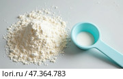 On a neutral background, a heap of white flour is displayed next to a light turquoise measuring spoon filled with sugar. This setup showcases baking ingredients. Стоковое AI-изображение, AI-художник Sergey Grishin / Фотобанк Лори