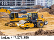 Heavy machinery for excavation and landscaping. Close-up view of an excavator and a road roller at a construction site. The excavator excavates the soil for excavation and construction. Стоковое фото, фотограф Photojuli / Фотобанк Лори